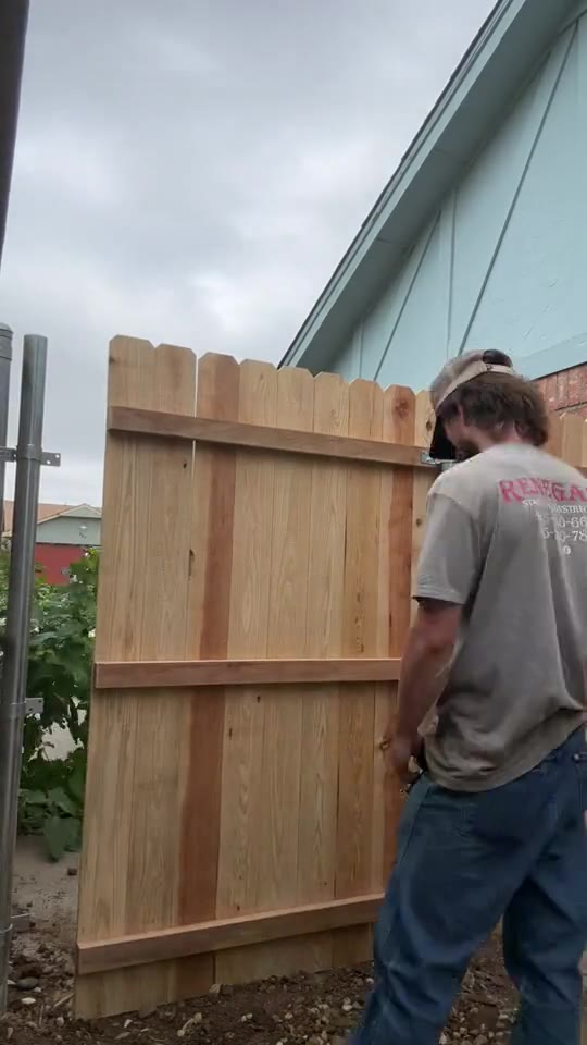 Installer checking the fit of a new wood gate beside a brick home